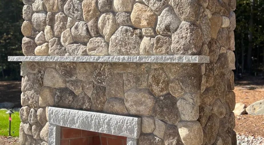 Outdoor stone fireplace construction with fieldstone on a backyard patio